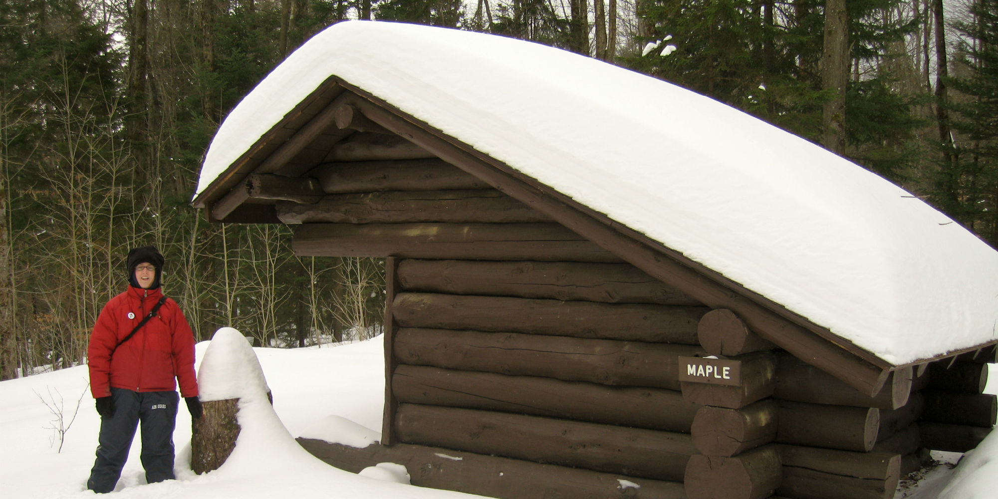 A winter camper stands next to a snowy leanto