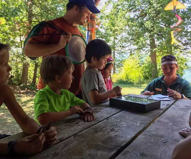A man smiling while standing next to his family at a picnic table at a Vermont State Park
