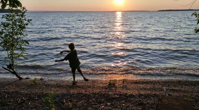 Boy skipping rocks at sunset at Kamp Kill Kare State Park by Laurie Briggs